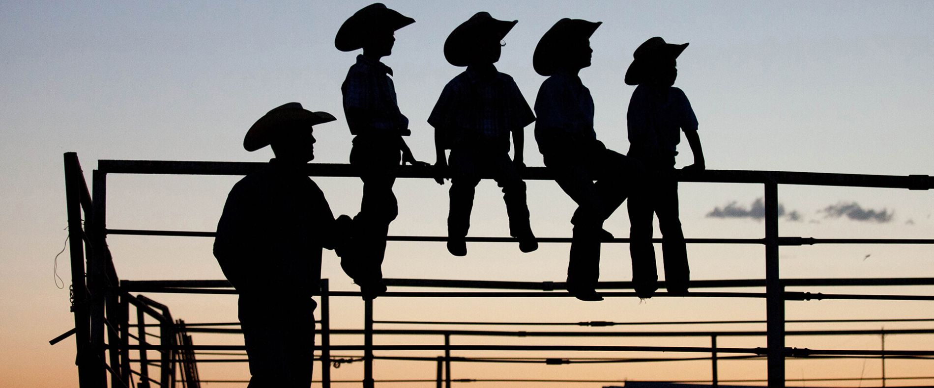 Rancher and boys sitting on a fence at sunset.